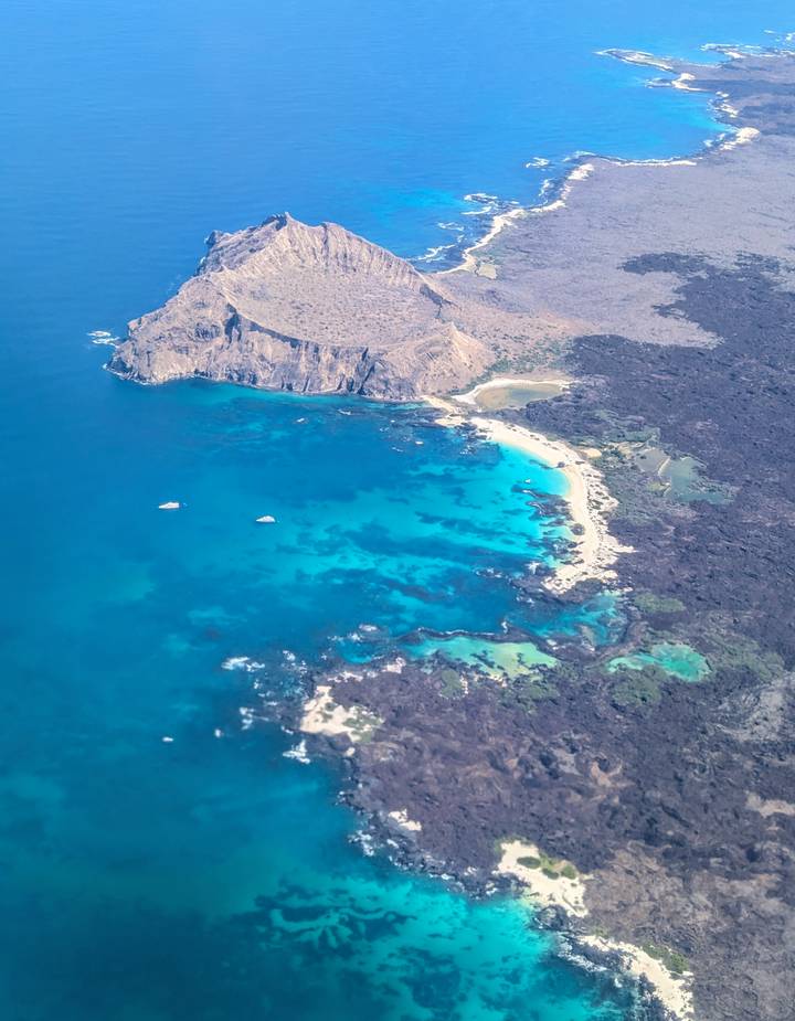 Aerial view of a turquoise bay, white sand beaches and dark volcanic coastline.
