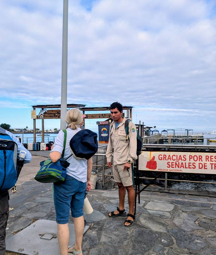 Travelers arriving at a pier with a welcome sign while a uniformed official looks on.