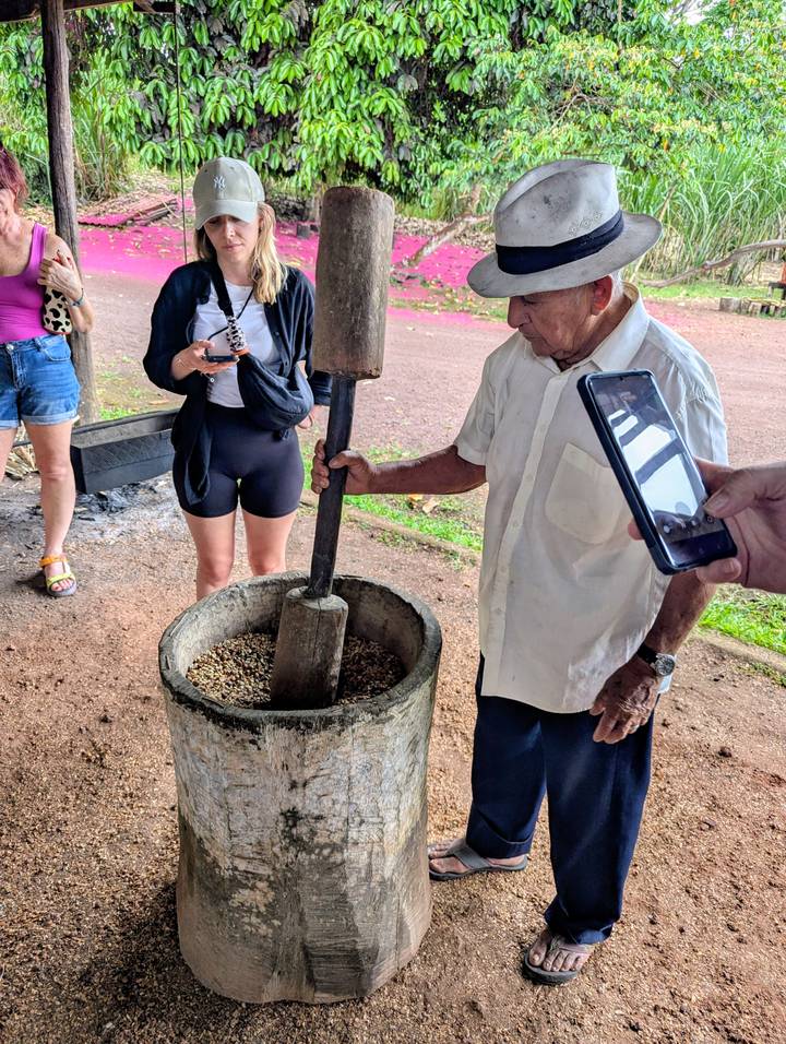 Local guide demonstrating traditional grinding of coffee beans while visitors observe and film.