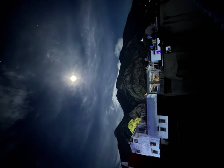 Night scene of moonlit mountains above blue-washed rooftops under scattered clouds.