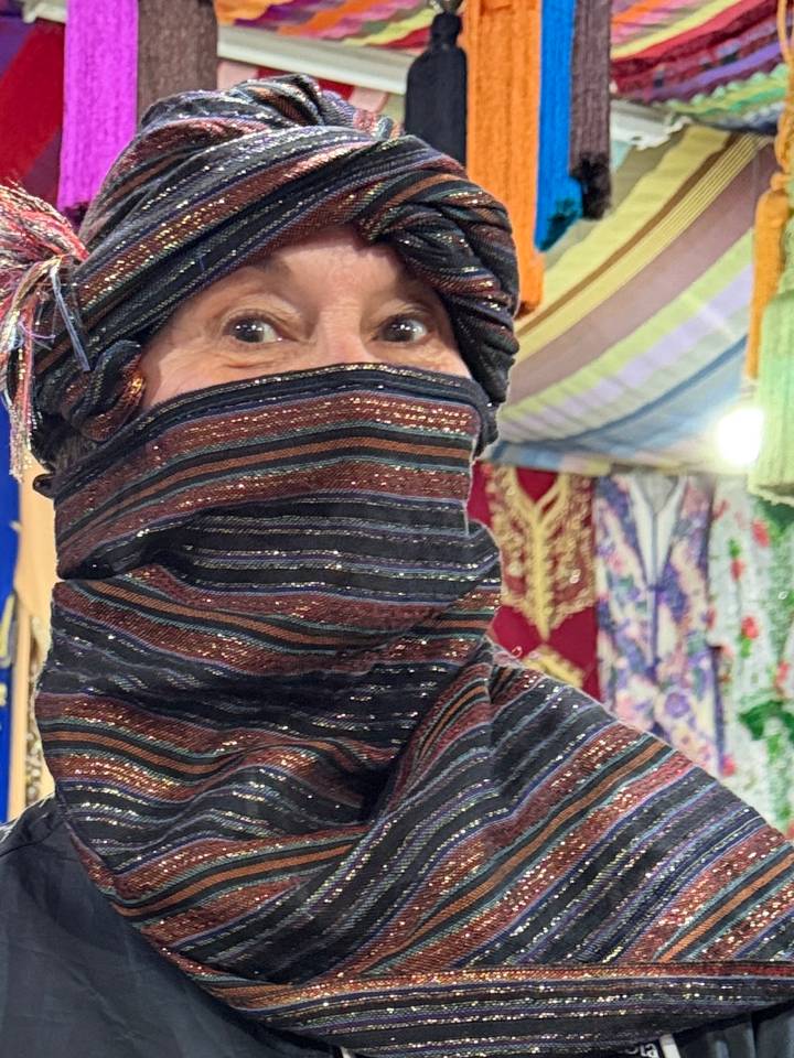 Close-up portrait of a woman wearing a colourful striped headscarf and face covering in a market stall.