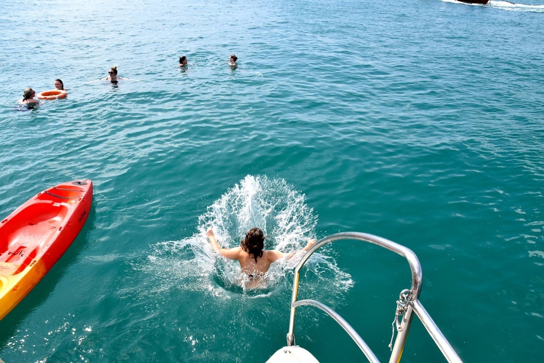 Personne plongeant d'un bateau dans la mer avec d'autres personnes nageant à proximité.