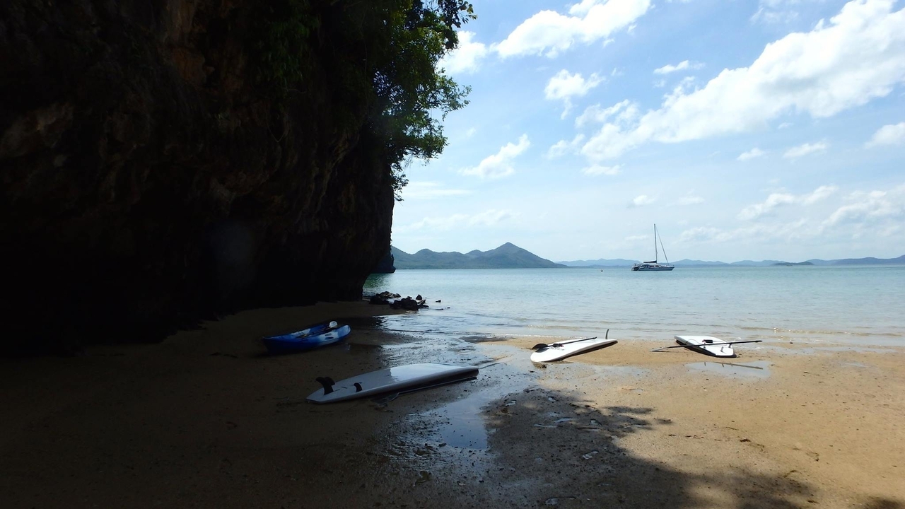 Plage vide avec des paddleboards et un yacht au loin par une journée ensoleillée.