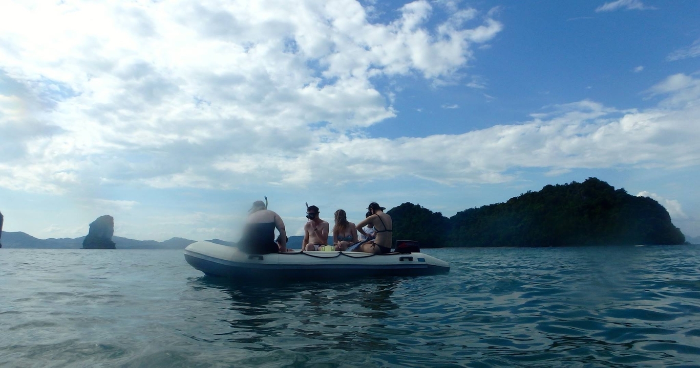 Quatre personnes assises dans un bateau pneumatique sur l'eau avec des îles montagneuses au loin.