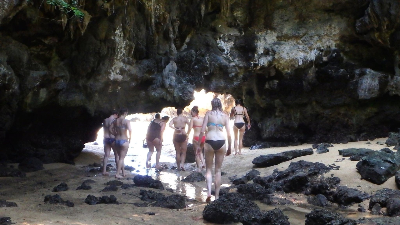 Personnes pénétrant dans une grotte sur une plage rocheuse.
