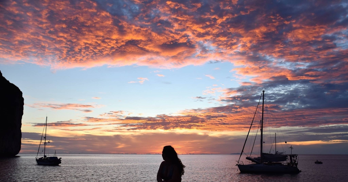Silhouette d'une personne sur fond de coucher de soleil coloré et de voiliers.