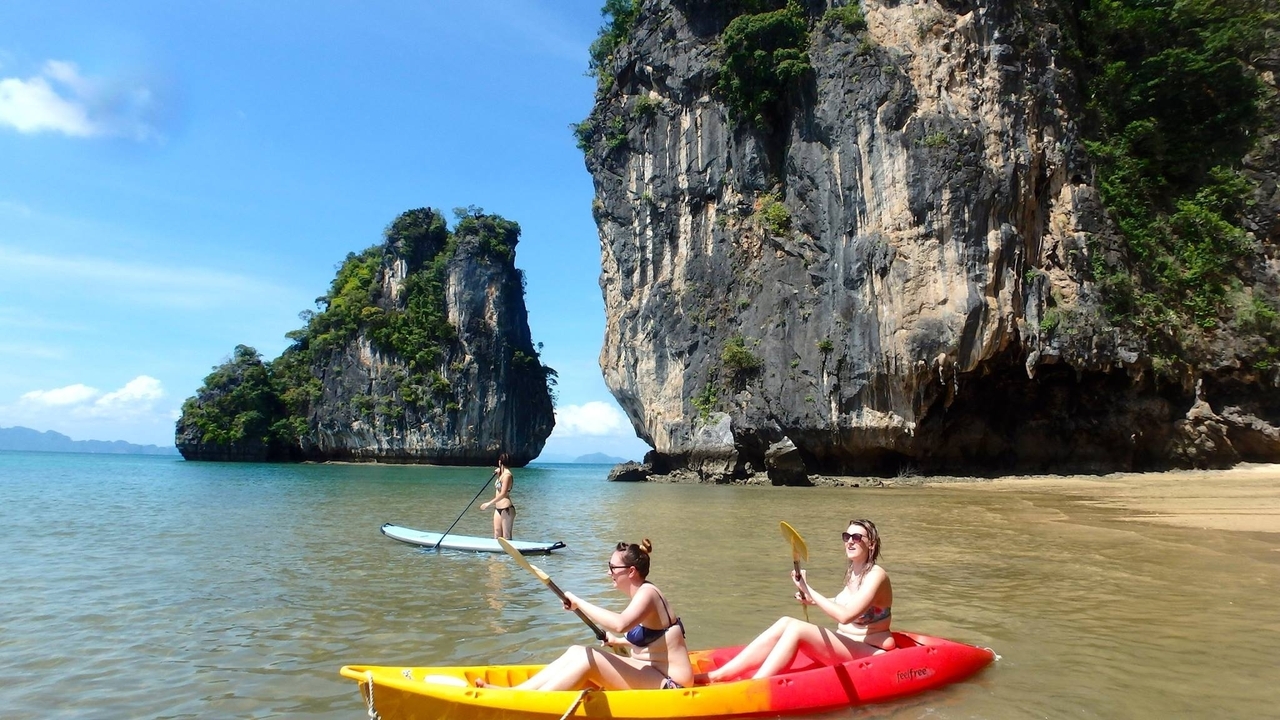 Deux personnes en kayak et une personne en paddleboard près de falaises calcaires par une journée ensoleillée.