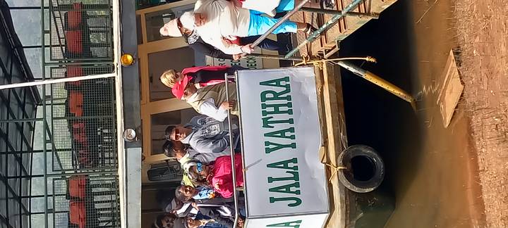 Tourists embark on a sightseeing boat named 'Jala Yathra' at a riverside jetty.