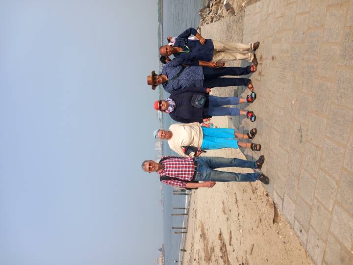 Group of travelers standing on a sandy walkway by the sea with hazy skyline in the distance.