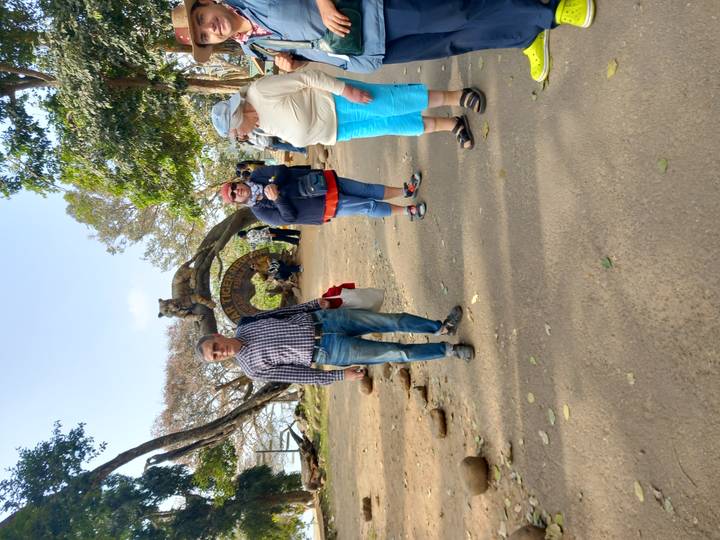 Travelers chat near the entrance sign of Periyar Tiger Reserve surrounded by trees.