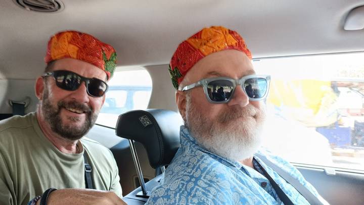 Two men wearing colourful Rajasthani caps smiling in a car interior.