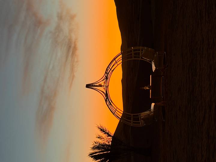 Artistic circular metal pavilion silhouetted against an orange desert sunset.