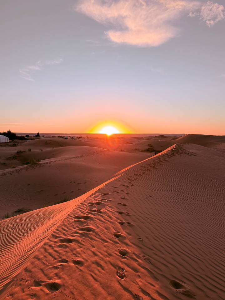 Golden sun rising over rolling Sahara dunes leaving soft footprints along the crest.