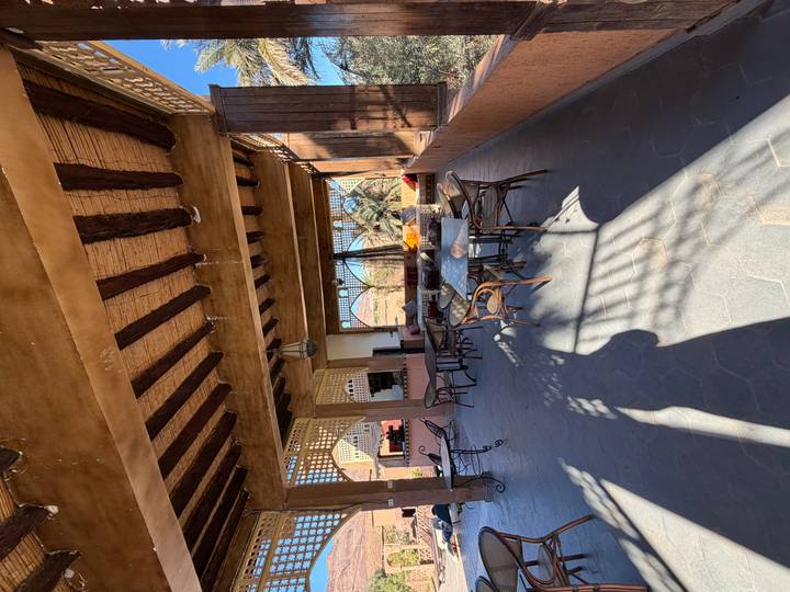 Shaded open-air lounge with rustic wooden beams, mosaic tables and desert views beyond.