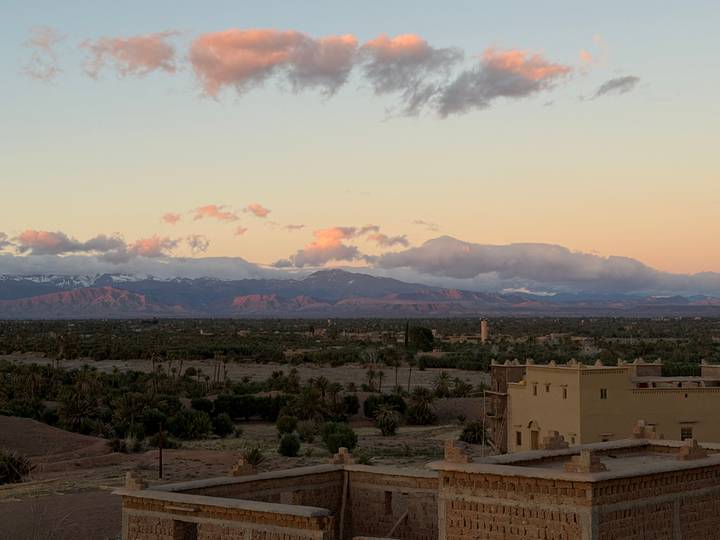 Wide view over a palm-filled valley toward snow-capped mountains glowing pink in the evening light, with an adobe tower in the foreground.