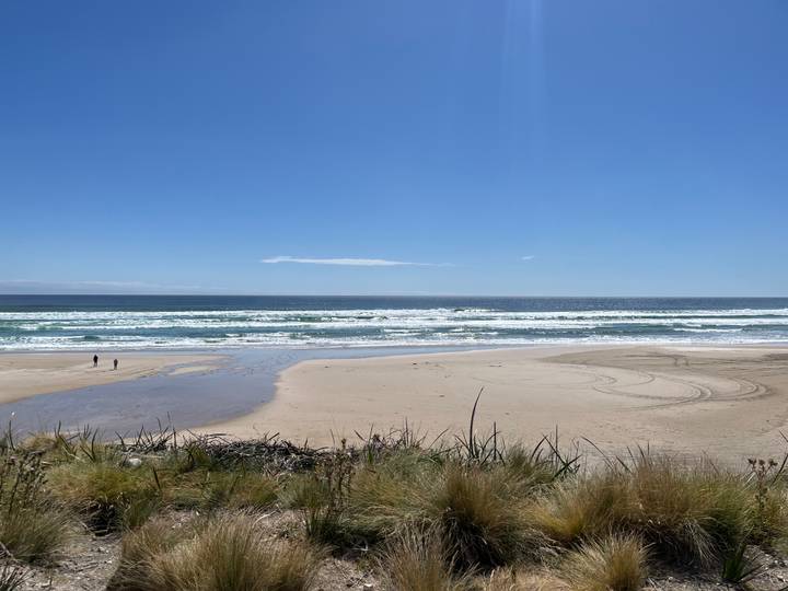 Wide sandy beach with two distant walkers beside rolling surf.
