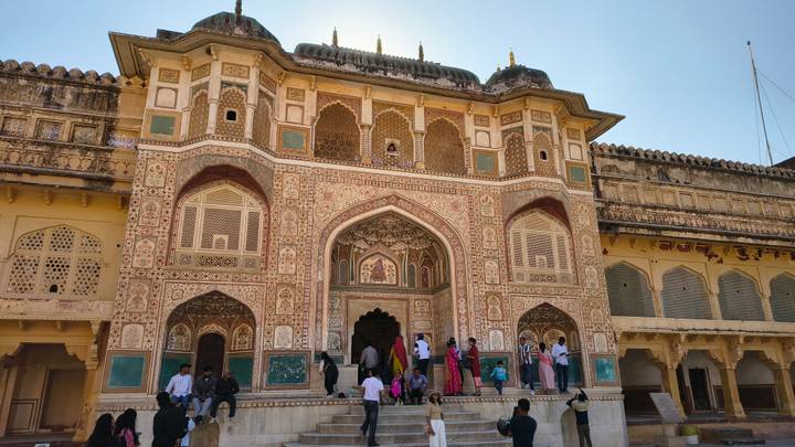 Intricately decorated gateway of Amber Fort with visitors on the steps.