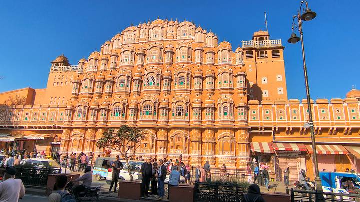 Iconic orange facade of Hawa Mahal bathed in bright morning light with bustling street below.