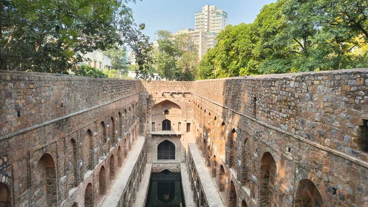 Stone stepwell with multi-level arches leading down to dark water in Delhi.