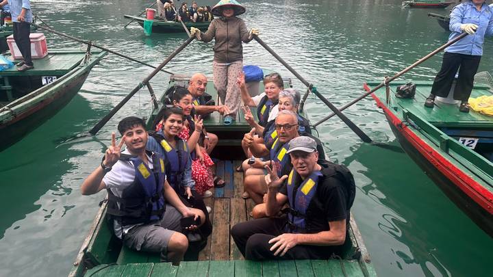 Tourists in life jackets posing on a small rowing boat in emerald water.