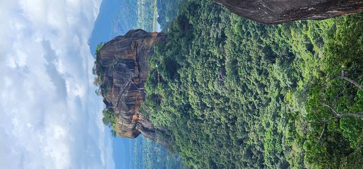Towering flat-topped Sigiriya rock fortress rises above dense tropical forest and distant mountains.