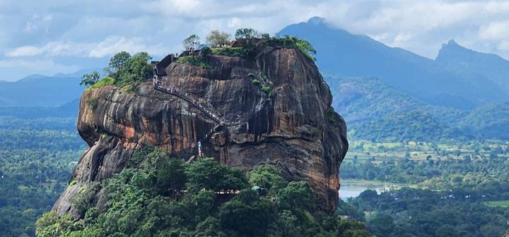 Close-up of Sigiriya rock showing switch-back staircases and lush landscape below.
