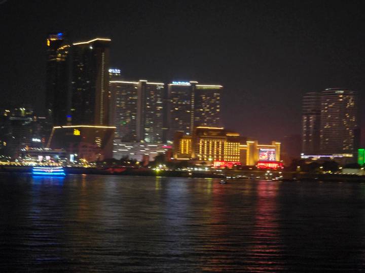 Blurry night skyline of a riverside city with brightly lit high-rise buildings reflecting on the water.