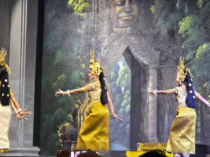Traditional Apsara dancers in ornate gold costumes performing on stage against an ancient-temple backdrop.