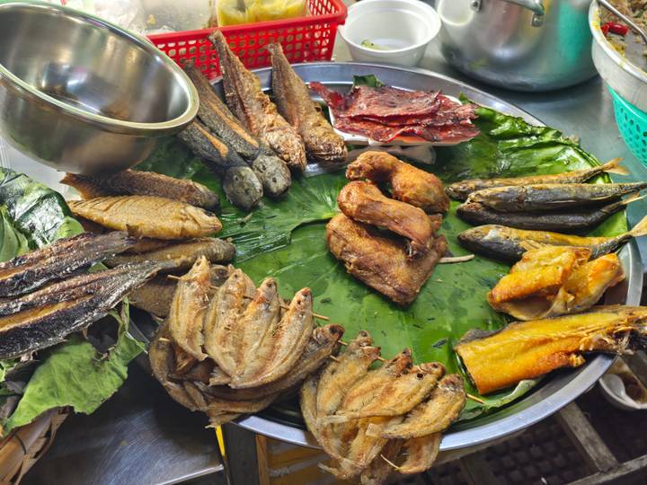 Assorted dried and cooked fish and poultry arranged on a banana-leaf lined tray at a local market stall.