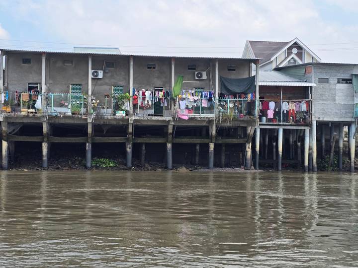 Stilt houses with laundry hanging over muddy river water in a riverside community.