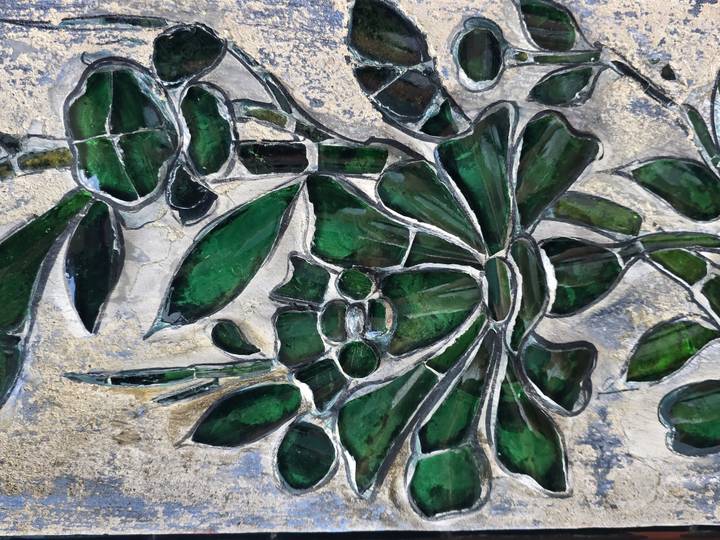 Close-up of stained-glass mosaic depicting green floral and bamboo motifs in earthy tones.