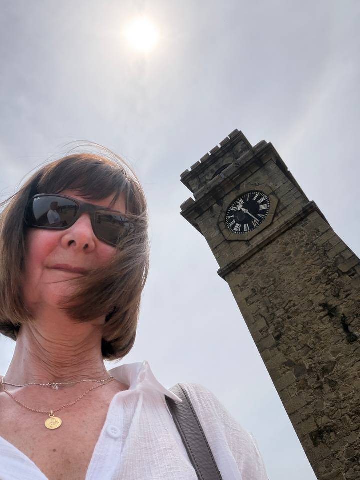 Selfie of a woman wearing sunglasses with the historic Galle Fort clock tower rising behind her against the sky.