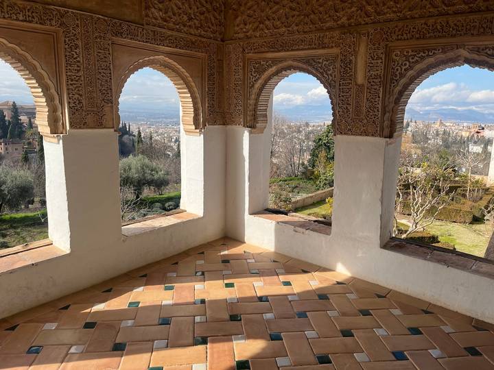 Intricate Moorish arches framing panoramic views over gardens and Granada from inside the Alhambra palace.