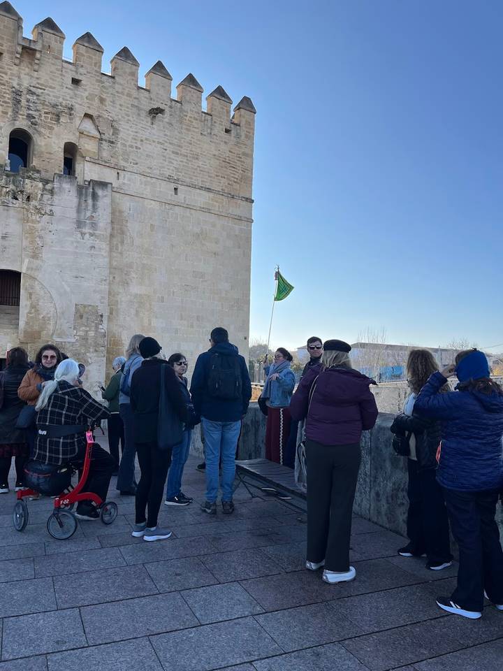 Tour group gathered outside a historic stone tower with a green flag fluttering on a sunny morning.
