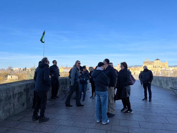 Tour group standing on a stone bridge overlooking Cordoba with the Mezquita cathedral visible in the distance.