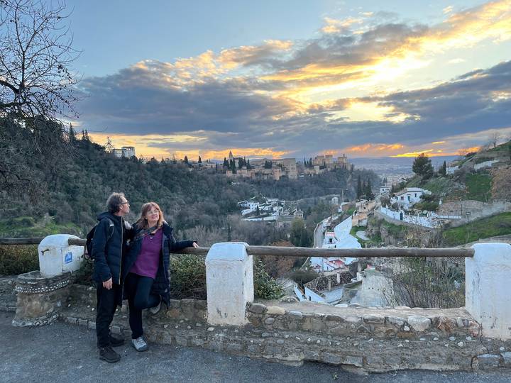 Couple at sunset viewpoint overlooking the Alhambra and Sierra Nevada mountains under dramatic skies.