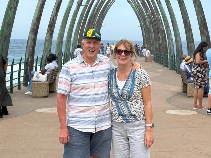 Smiling couple posing on a curving seaside pier with the Indian Ocean in the background.