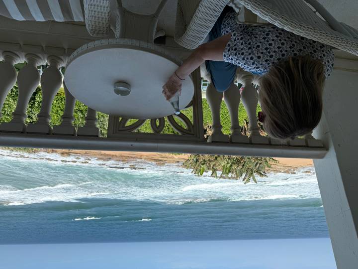 Woman relaxing on a balcony with drink in hand overlooking waves crashing on a sandy beach.