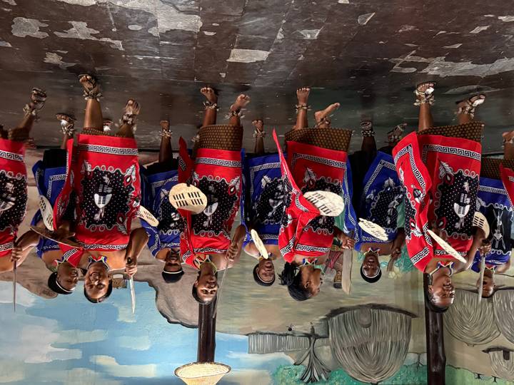 Vibrant troupe of women in colorful traditional attire performing an energetic dance with shields and sticks.