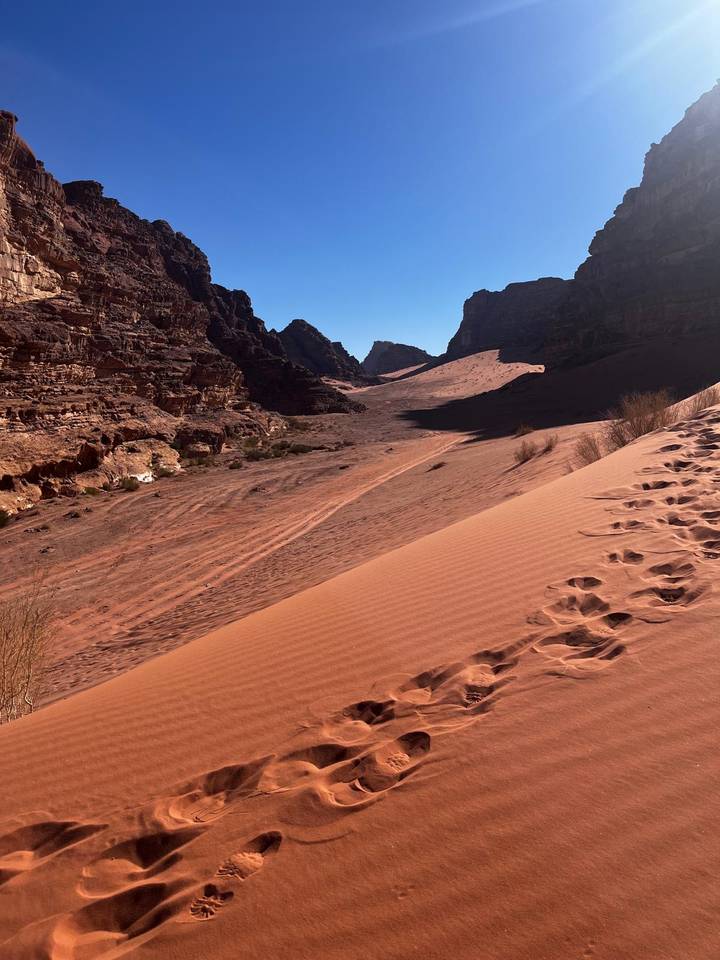 Rippling sand dunes and rocky cliffs of Wadi Rum marked with fresh footprints.