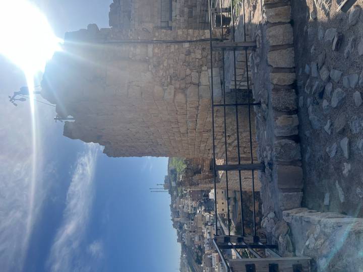 Sun flare peeks over the stone walls of a hilltop Jordanian fortress overlooking a town below.