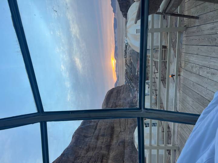 Sunrise view from inside a glass-front desert dome looking out to a Wadi Rum camp and rocky horizon.