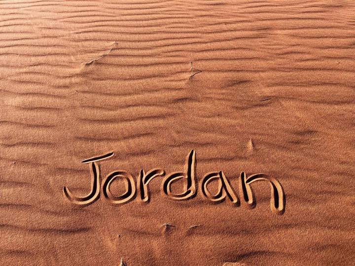 The word 'Jordan' handwritten in rippled red desert sand.