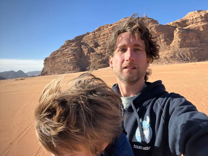 Travel selfie of a man holding a child in the wide orange sands of Wadi Rum.