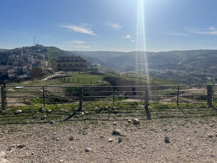 Hilltop ruins and surrounding town viewed across a fenced overlook on a sunny day.