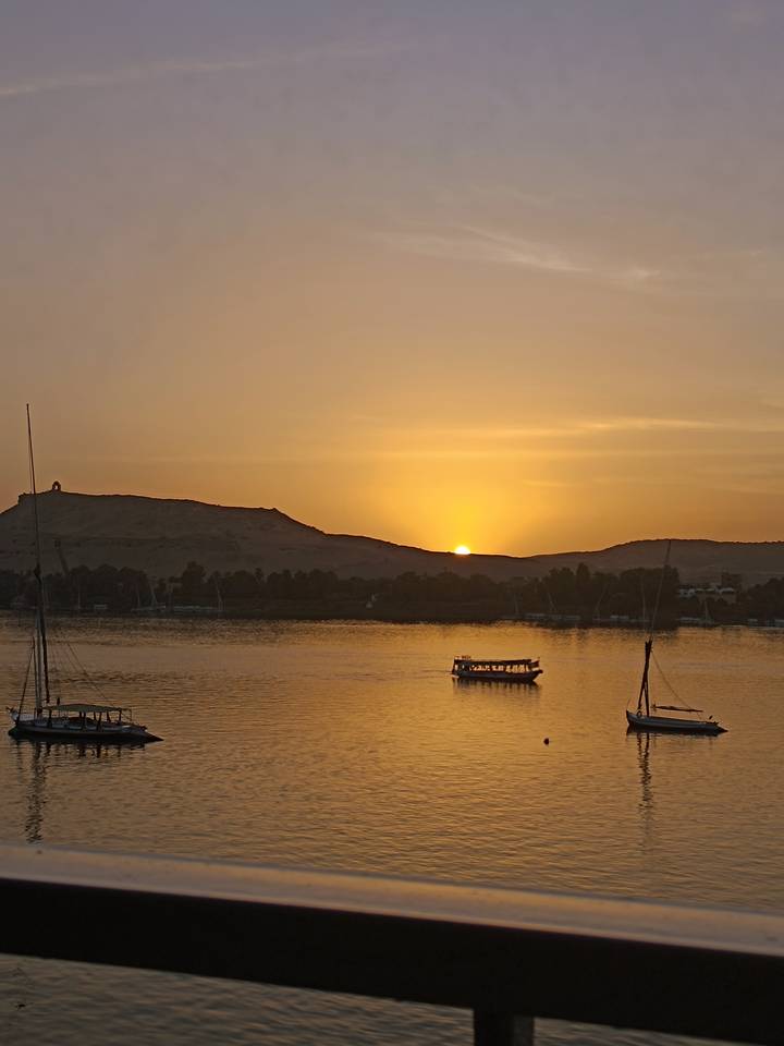 Golden sun setting behind desert ridge over the Nile with felucca silhouette.