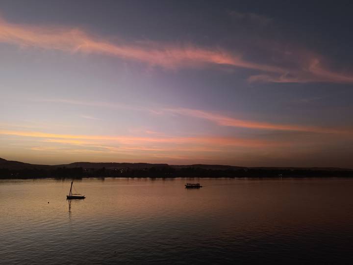 Pastel twilight sky reflected on calm Nile waters with small sailboats anchored.