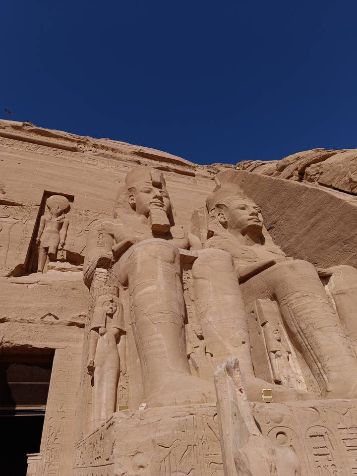 Colossal seated statues of Abu Simbel carved from sandstone cliff under deep blue sky.