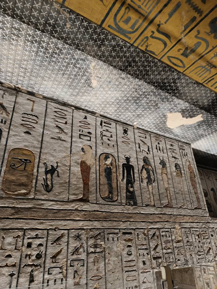 Close-up view of ancient Egyptian hieroglyphs and painted deities on a tomb ceiling and wall.
