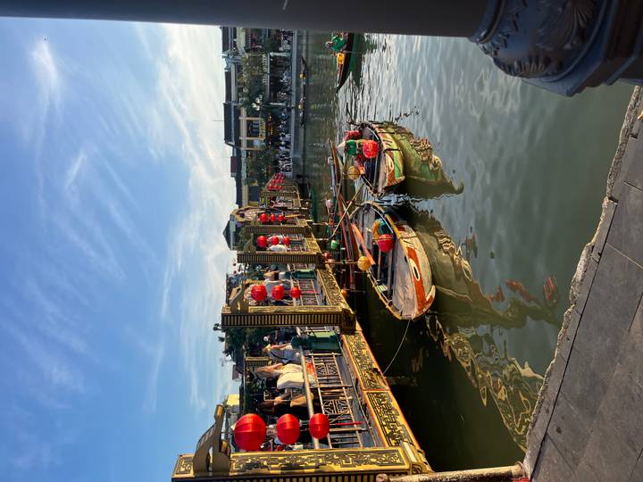 Traditional wooden boats decorated with lanterns float on a bustling canal in Hoi An at sunset.